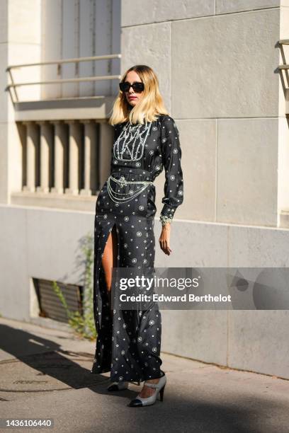 Guest wears black sunglasses, a black with white CC logo print pattern / embroidered white crystal chest / silk long blouse dress from Chanel, a...