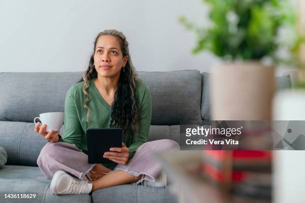 full length view of young woman connected with technology searching online at home in the couch. - vita domestica fotografías e imágenes de stock