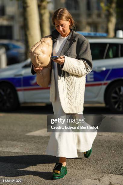 Guest wears silver earrings, a white long dress, a gray blazer jacket and white latte braided wool pullover bi materials jacket, a beige shiny...