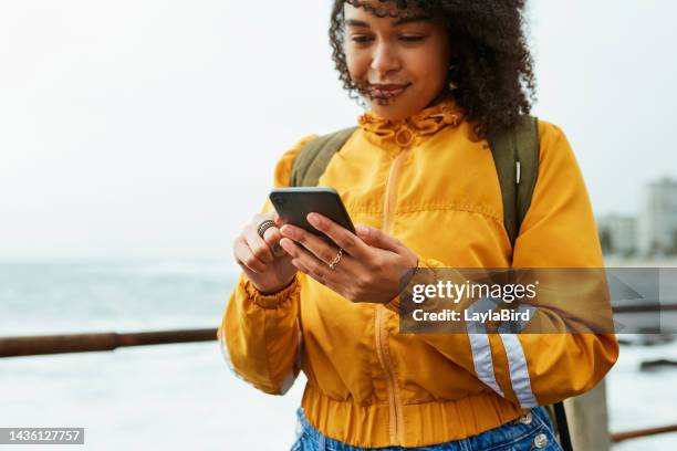 mädchen, telefon und lächeln lesen soziale medien, kommunikation oder text am meer. schwarze frau und smartphone für e-mail, soziales netzwerk oder sms in der natur, wind und meer chat im web, internet oder app - in real life stock-fotos und bilder