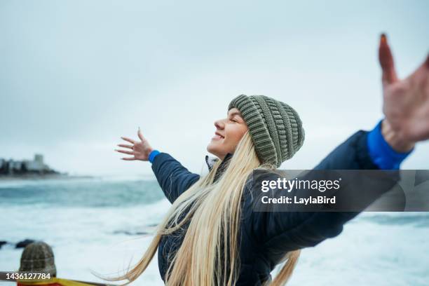 freedom, nature and woman at the beach in winter, happy and cheerful along the ocean on a cold morning. travel, earth and lady celebrating vacation and sea trip, connected to earth and spiritual - hand on head stockfoto's en -beelden