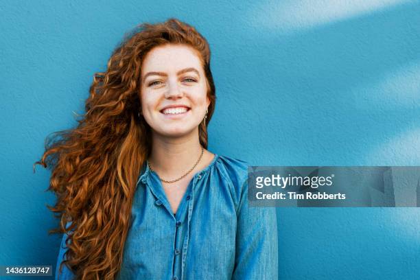 portrait of happy woman next to blue wall - natuurlijk haar stockfoto's en -beelden