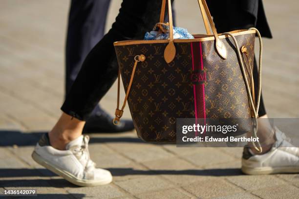 Guest wears black suede pants, a brown LV monogram in coated canvas Neverfull handbag from Louis Vuitton, white leather sneakers, outside Louis...