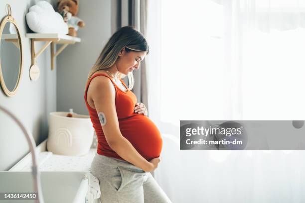 mujer joven embarazada con diabetes en casa sintiéndose emocionada por su primogénito - embarazada fotografías e imágenes de stock