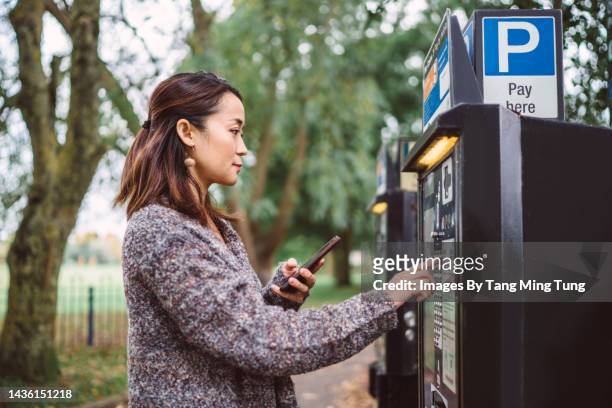 young pretty asian woman making contactless payment with smartphone at parking payment machine in city street - パーキングメーター ストックフォトと画像