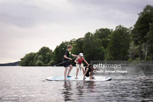 siblings falling from paddle board on lake - paddleboard stock pictures, royalty-free photos & images