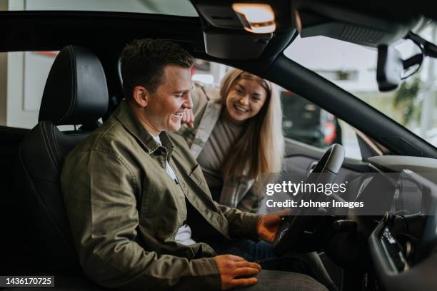 young couple testing car in car dealership - car ownership fotografías e imágenes de stock