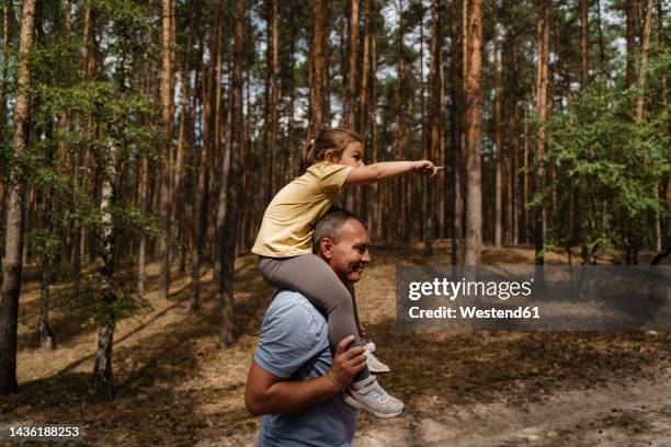 mature man carrying girl on shoulders and walking in forest - 肩車 ストックフォトと画像