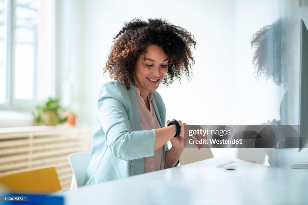 Smiling businesswoman with curly hair checking time on smart watch at office