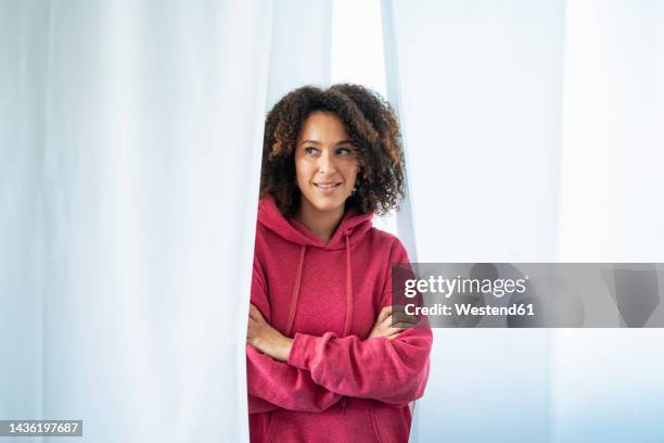 thoughtful woman with arms crossed amidst white curtains - lila stockfoto's en -beelden