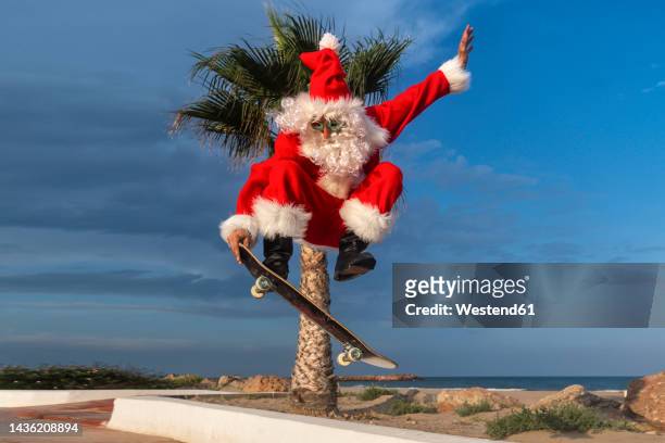 mature man wearing santa claus costume skateboarding on footpath - claus lange stock pictures, royalty-free photos & images