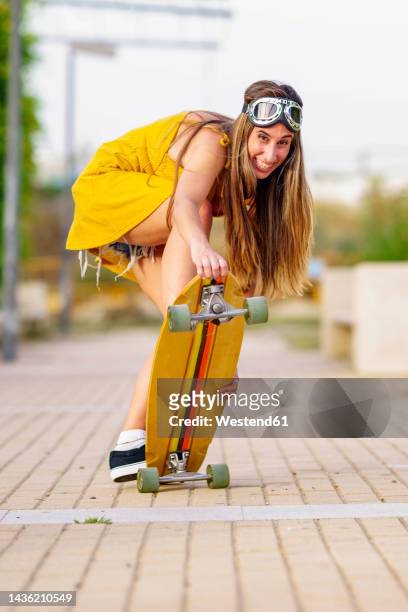happy woman with long hair skateboarding on footpath - flying goggles photos et images de collection