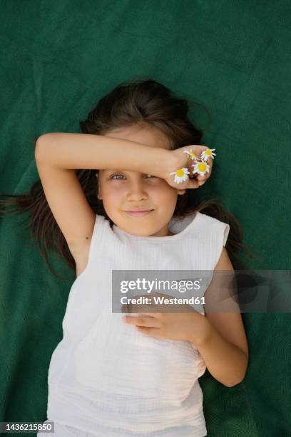 smiling girl holding chamomile flowers lying on blanket - supino foto e immagini stock