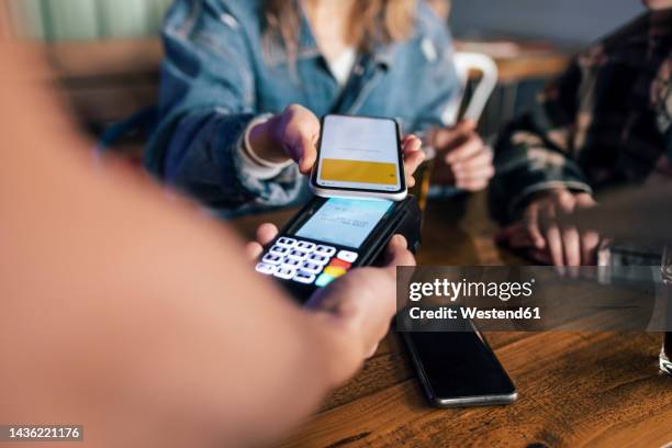 young woman paying bill through smart phone at restaurant - brand name mobile payment photos et images de collection