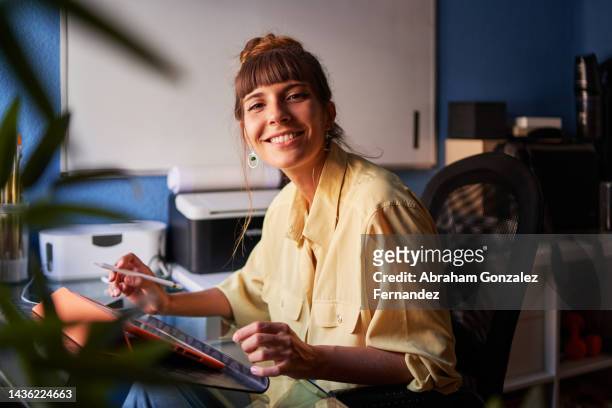 a graphic designer working from home with her digital tablet looking at the camera and smiling - femme et sourire photos et images de collection