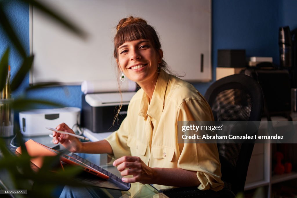 A graphic designer working from home with her digital tablet looking at the camera and smiling