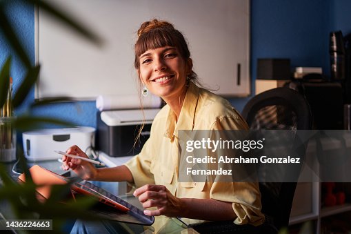 A graphic designer working from home with her digital tablet looking at the camera and smiling A graphic designer working from home with her digital tablet looking at the camera and smiling