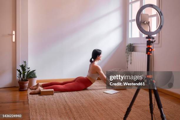 young woman doing cobra pose yoga teaching online using smart phone at home - ring light stock pictures, royalty-free photos & images