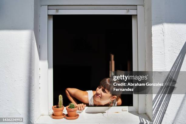 a young woman sticking her head out of the window and looking to the side - bad neighbor foto e immagini stock