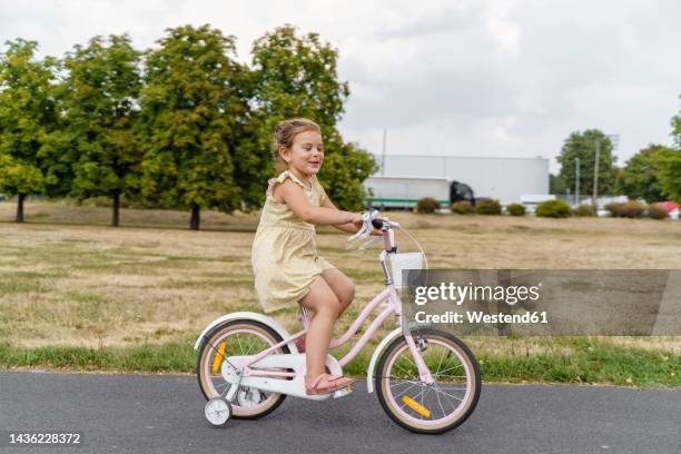 smiling girl riding bicycle at park - training wheels stock pictures, royalty-free photos & images