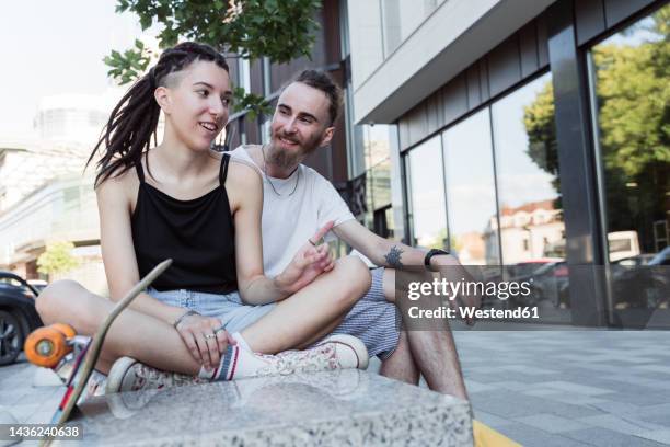 non-binary person sitting cross-legged on bench talking to man - non urban scene stockfoto's en -beelden
