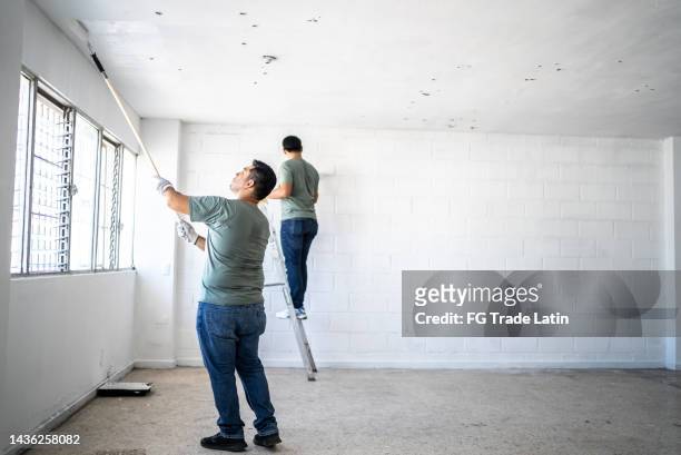 young painter - construction worker painting the ceiling indoors - painter in overhauls bildbanksfoton och bilder