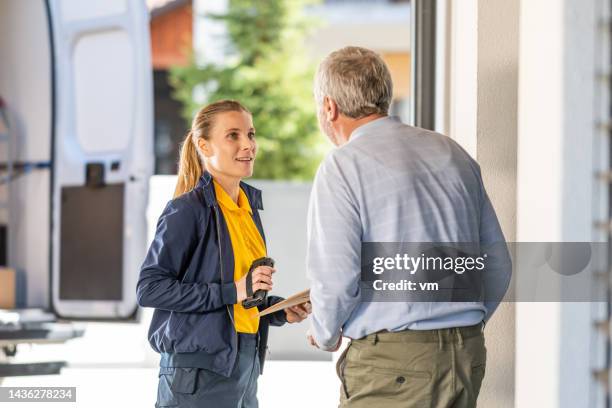 young postal worker giving senior man envelope package, medium shot - postbode stockfoto's en -beelden