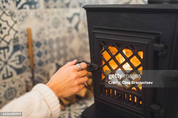 woman hand opening wood-burning vintage metal stove. cozy fireplace at home. - wood burning stove stock-fotos und bilder