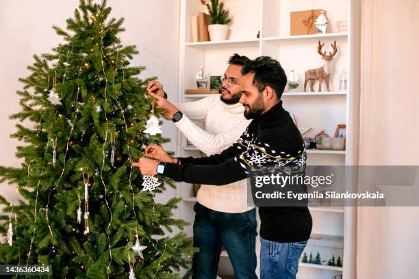 two indian men decorating christmas tree at home. - decorating the christmas tree stock pictures, royalty-free photos & images