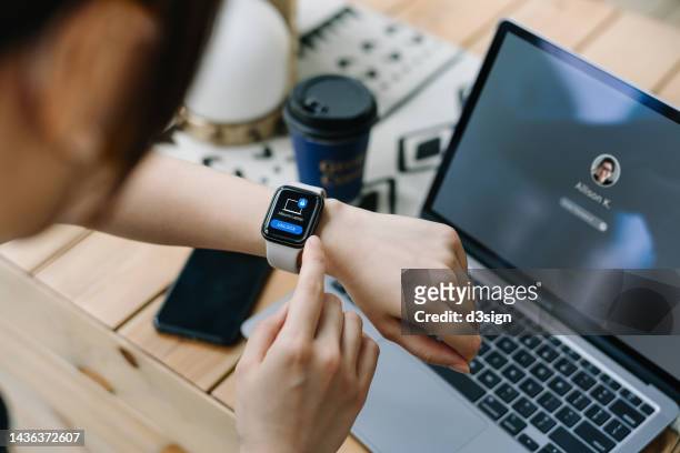 over the shoulder view of young asian woman using smartwatch with two-factor authentication (2fa) security to unlock and logging in securely to her laptop. privacy protection, internet and mobile security - identity theft stockfoto's en -beelden