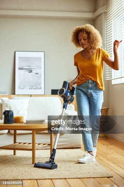 woman using vacuum cleaner in living room at home - vacuum cleaner woman stockfoto's en -beelden