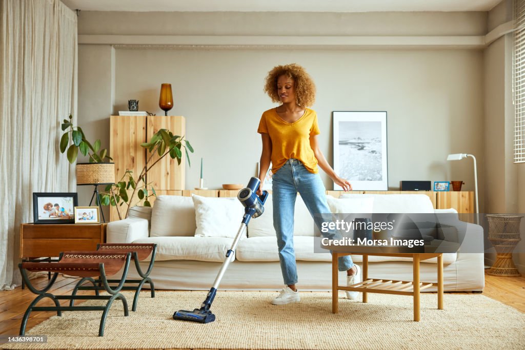 Woman cleaning carpet with vacuum cleaner at home
