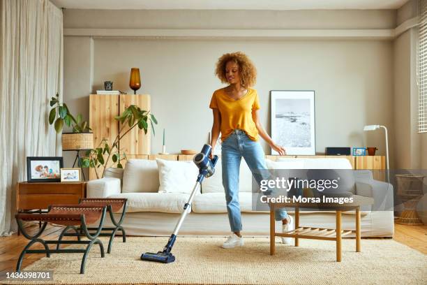 woman cleaning carpet with vacuum cleaner at home - chores stock-fotos und bilder