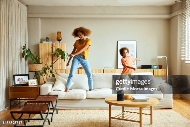 happy mother and son dancing on sofa at home - case foto e immagini stock