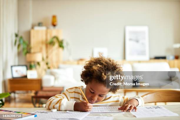 african american boy with pencil writing on paper at table - e learning draw stock pictures, royalty-free photos & images