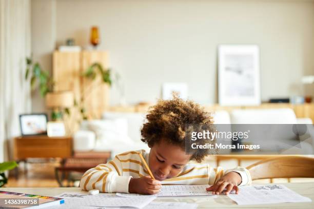 african american boy with pencil writing on paper at table - ensino doméstico imagens e fotografias de stock