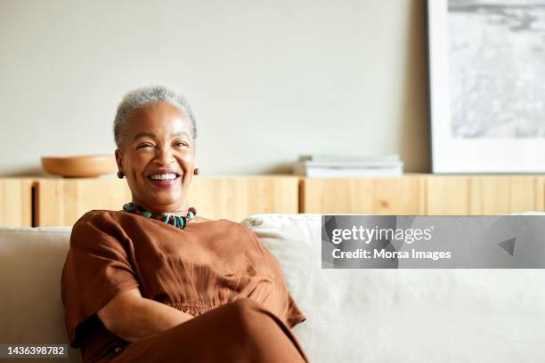 portrait of happy senior woman sitting on sofa - middle aged woman ストックフォトと画像