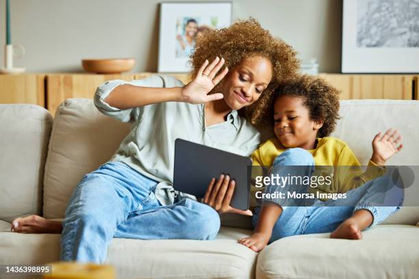 mother and son waving at tablet pc in living room - family tablet stock pictures, royalty-free photos & images