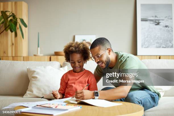 man helping son in doing homework at coffee table - kids reading glasses stock pictures, royalty-free photos & images