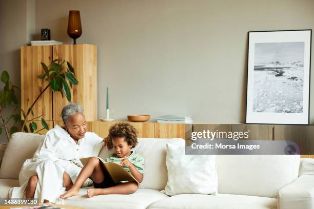 senior woman looking at boy reading picture book - casa real española fotografías e imágenes de stock