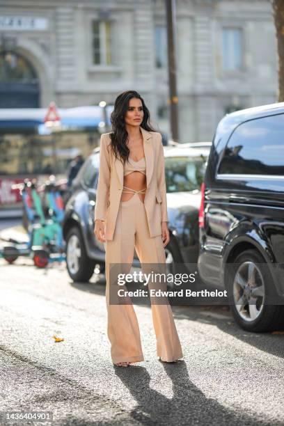 Guest wears gold earrings, a beige linen V-neck / cropped top, a beige linen blazer jacket, matching beige linen with laces waist / flared suit...