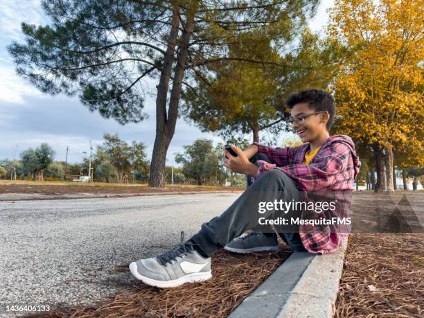 niño usando un teléfono inteligente en el parque público - southern europe fotografías e imágenes de stock