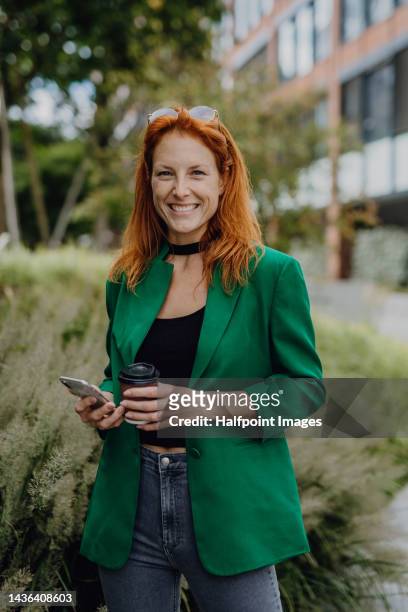 young redhead woman walking in city with phone and cup of coffee. - coffee chat stockfoto's en -beelden
