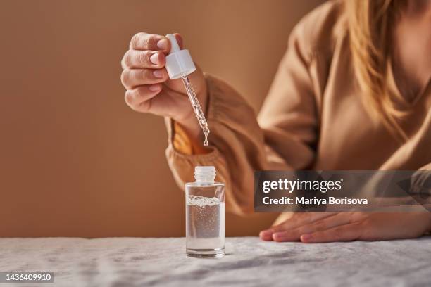 a girl in a beige dress holds a pipette with a drop of serum in her hands. - pipette stock pictures, royalty-free photos & images