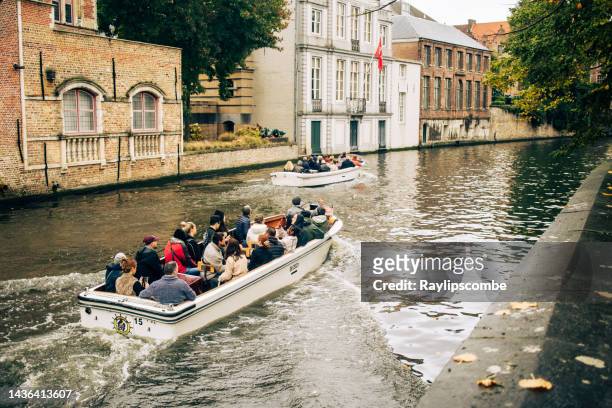 tourists exploring the stunning and beautiful medieval architecture of the town of bruges in belgium on a small canal tour boat on a damp autumn/fall day - turistbåt bildbanksfoton och bilder