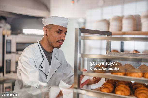 professional baker looking at the quality of the croissants in the kitchen - french boulangerie stock pictures, royalty-free photos & images