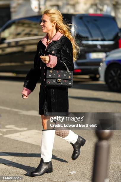 Guest wears a white pearls necklace, a pale pink tweed jacket, a black velvet ribbed long coat from Chanel, a black fabric with multicolored pearls...