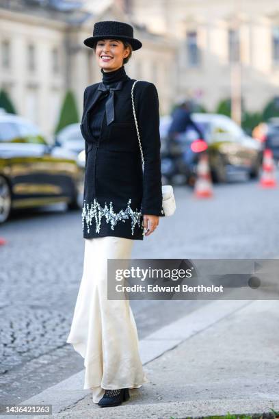 Guest wears a black tweed hat, a black ribbed wool turtleneck pullover, a black tweed / zipper / embroidered silver crustal and sequined borders...