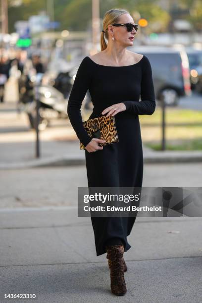 Guest wears black sunglasses, gold and pearl pendant earrings, a black long sleeves / long dress, a yellow orange and black leopard print pattern fur...