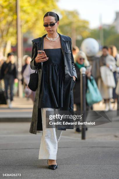 Guest wears black sunglasses, white pearls earrings, a white pearls necklace, a black shoulder-off / pleated long top, a black shiny leather long...